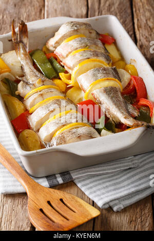 Merluzzo bianco intero cotto con pepe, pomodori, cipolle e limone in una teglia da forno da vicino sul piano verticale. Foto Stock