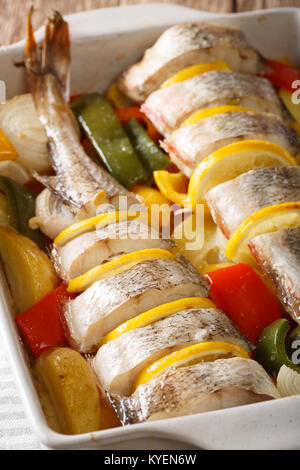 Merluzzo bianco intero cotto con verdure e limone in una teglia da forno da vicino sul piano verticale. Foto Stock