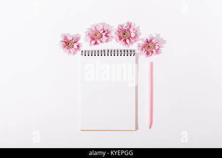 Blocco note con una matita e fiori di colore rosa su un tavolo bianco vista superiore Foto Stock