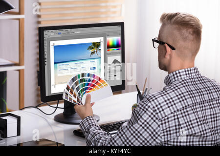 Un Designer maschio utilizzando Computer tenendo i campioni di colore in mano Foto Stock