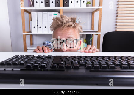 Imprenditore divertenti indossando occhiali nascondendo dietro la scrivania in ufficio Foto Stock