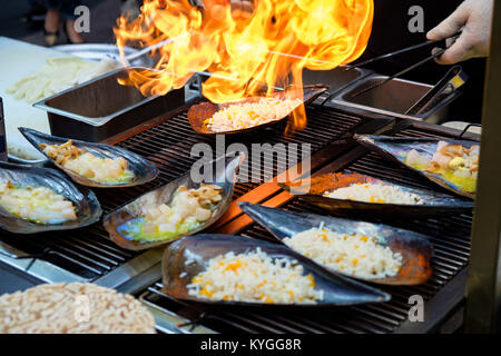 Fresco tritato Atrina pectinata, con il formaggio sulla parte superiore, sono cucinati da un lanciafiamme (Coreano street food) Foto Stock