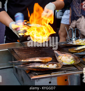 Fresco tritato Atrina pectinata, con il formaggio sulla parte superiore, sono cucinati da un lanciafiamme (Coreano street food) Foto Stock