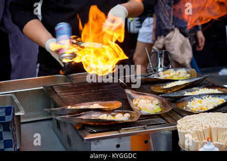 Fresco tritato Atrina pectinata, con il formaggio sulla parte superiore, sono cucinati da un lanciafiamme (Coreano street food) Foto Stock