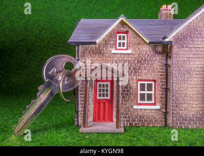 La chiave per la porta appoggiato su di un modello di casa. Concetto relativo alla home occupazione, ad esempio, acquisto / vendita / Locazione / movimento / ipoteca. Foto Stock
