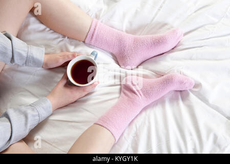 Mani tenendo una tazza di caffè. È possibile vedere le gambe in rosa calze. Foto Stock