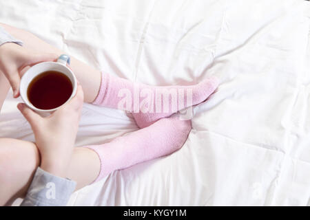 Mani tenendo una tazza di caffè. È possibile vedere le gambe in rosa calze. Foto Stock