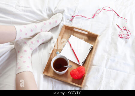 Un vassoio con una tazza di caffè, un blocco per appunti e una matita si erge sul letto Foto Stock