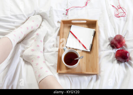 Un vassoio con una tazza di caffè, un blocco per appunti e una matita si erge sul letto Foto Stock