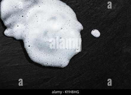 Bianco di schiuma di sapone liquido sul nero testurizzato piastrella per pavimenti, bolle. Foto Stock