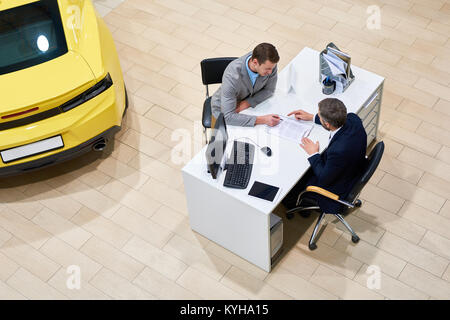 Al di sopra di vista del giovane uomo bello lettura del contratto di acquisto seduto alla scrivania in concessionaria shop prima di acquistare auto di lusso, spazio di copia Foto Stock