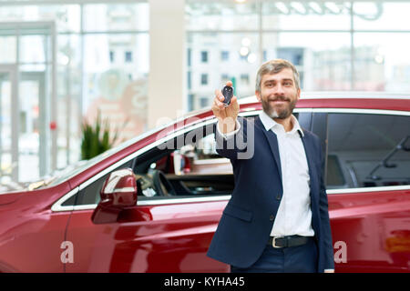 Ritratto di bella coppia uomo sorridente felicemente in telecamera in piedi dal nuovissimo hotel di lusso auto in showroom e presentando le chiavi dell'auto, spazio di copia Foto Stock