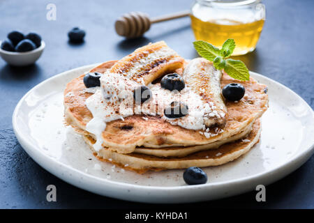 Frittelle di avena con yogurt greco, arrosto di banana, mirtilli e cannella sulla piastra bianca Foto Stock