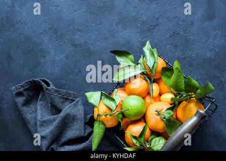 Mandarini o clementine con foglie verdi nel cesto su sfondo scuro. Vista superiore e copiare lo spazio per testo Foto Stock