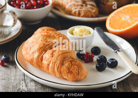 Croissant con frutti di bosco freschi e burro. Caffè, bacche e frutti sullo sfondo. Concetto di colazione continentale. Primo piano Foto Stock