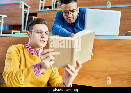 Ritratto di due studenti discutendo lecture seduti nella sala prima classe, concentrarsi su yping uomo che indossa gli occhiali azienda libro aperto Foto Stock