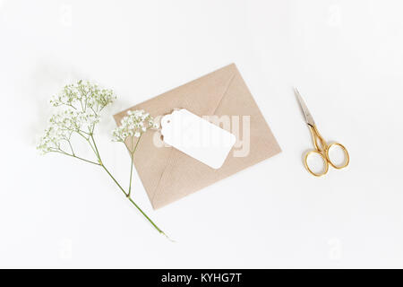 Bianco tag regalo con carta craft busta, golden forbici e bimbo di respiro Gypsophila fiori isolati su bianco sullo sfondo della tabella. Il matrimonio o un compleanno in stile foto stock, vista superiore piana e composizione di laici. Foto Stock