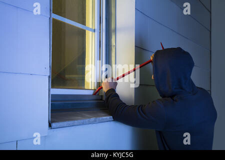 Close-up di rapinatore nel cofano usando il piede di porco Rosso Per aprire la finestra in vetro Foto Stock
