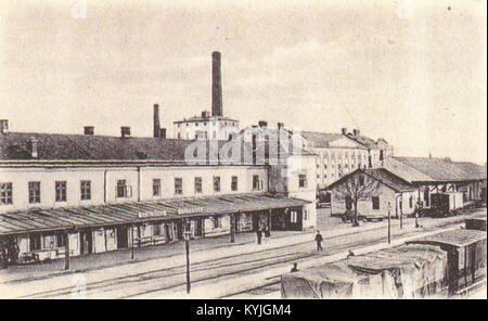 La fotografia raffigura un impianto di produzione dello zucchero con una stazione adiacente. L'immagine illustra l'architettura industriale e la logistica della produzione di zucchero, mostrando le aree di stoccaggio, i binari di trasporto e le strutture di fabbrica. Foto Stock