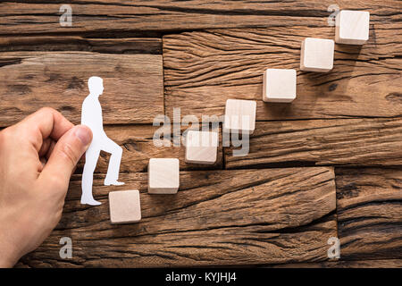 Close-up di Stepping a mano la carta tagliata fuori la figura sulla crescente blocchi disposti Foto Stock