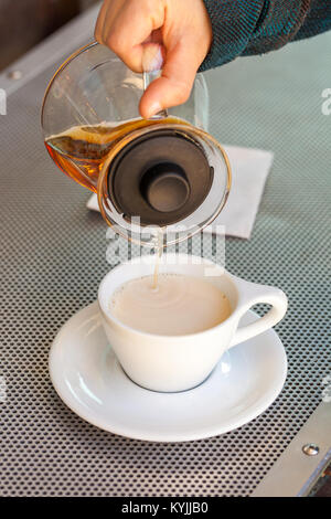 Donna mano versa il tè nero dal vetro teiera in tazza di ceramica Foto Stock