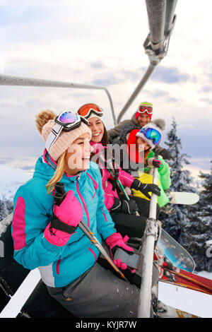 Allegro amici giovani sciatori su sci lift di salire sulla pista da sci in giornata nevosa Foto Stock