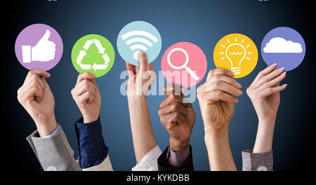 Gli imprenditori mani tenendo vari simboli aziendali contro lo sfondo blu Foto Stock