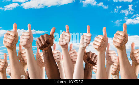 Molte mani che mostra il pollice in alto segno contro il cielo blu Foto Stock