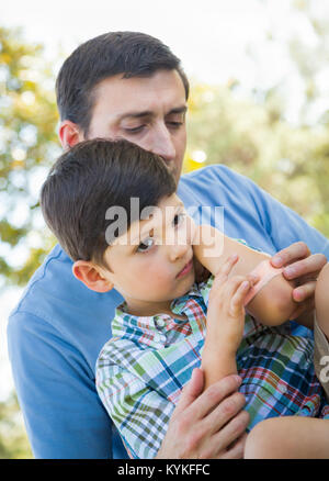 Padre amorevole mette una benda sul gomito del suo giovane figlio nel parco. Foto Stock