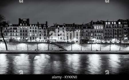 Paris panorama notturno di edifici illuminati lungo il Fiume Senna con riflessi nell'acqua sottostante. Poche persone. In bianco e nero con una copia dello spazio. Foto Stock