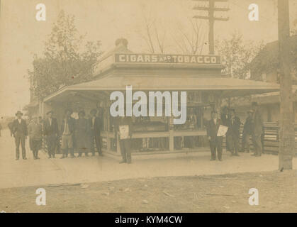 Una scena storica che raffigura una folla riunita in un'edicola di Hillsboro, Texas. L'immagine cattura l'atmosfera vivace dei venditori di notizie e dell'area circostante in passato, mostrando padiglioni in vecchio stile e l'ambiente di strada affollato. Questa foto è di un'epoca passata, che evoca un senso di nostalgia e storia. Foto Stock