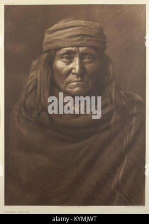 Questo storico ritratto di Edward Curtis raffigura un uomo nativo americano della tribù Apache. L'immagine cattura il soggetto in abiti tradizionali, evidenziando il lavoro di Curtis nella documentazione della cultura e della storia dei nativi americani durante i primi anni del XX secolo. Foto Stock