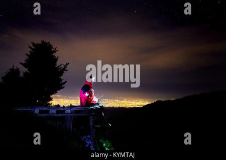 Bagnino di giacca rossa con croce medica ubicazione sul ramo di legno in mountain ski resort con vista di notte la luce della città Foto Stock