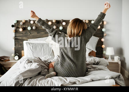 Vista posteriore della donna stretching nel suo letto Foto Stock