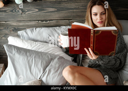 Donna interessati con il caffè del mattino la lettura di un libro a bedrooom Foto Stock