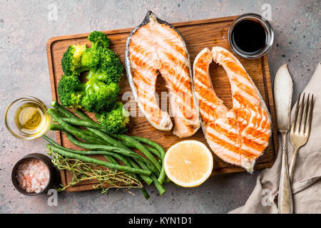 Tagliere con salmone alla griglia bistecche e verdure su tabella grigia, vista dall'alto Foto Stock