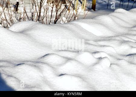 Puffy, poco gobbe di neve soffiata su una strada di fronte al sole nel pomeriggio. Prese su gennaio 13, 2018 a 3:20 PM. Foto Stock