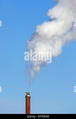 Camino industriale / smoke stack fumaiolo / contro il cielo blu su un giorno windless Foto Stock