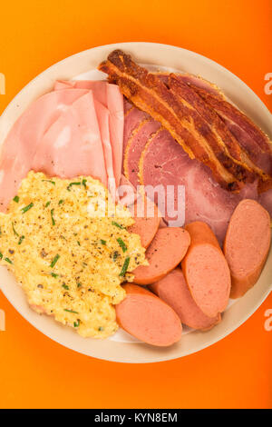 Svedese o in stile Norvegese le uova strapazzate, salsiccia pancetta e prosciutto Colazione contro uno sfondo arancione Foto Stock