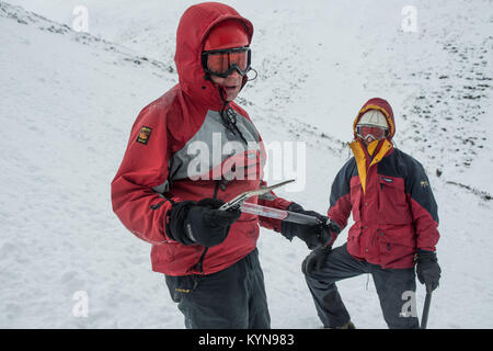 In inverno la formazione di competenze in Cairngorm montagne prima neve viaggio di foratura. Andy dimostrando l'uso di una piccozza - con Wayne dietro. Foto Stock
