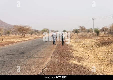 Vista posteriore di due uomini africani a piedi lungo una strada di campagna, il Sahel, nel nord del Burkina Faso, Africa occidentale Foto Stock