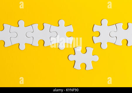 White jigsaw puzzle pezzi su uno sfondo giallo. Business del concetto di soluzione Foto Stock