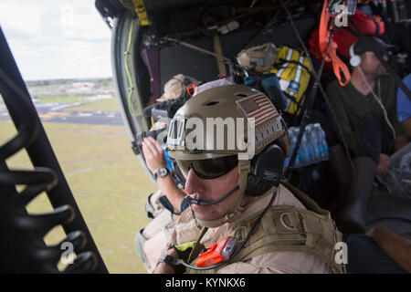 Stati Uniti Delle dogane e della protezione delle frontiere aria e operazioni Marine Aviation esecuzione Agent Mickey Hohol siede nella porta aperta di un Black Hawk elicottero come lui e i suoi compagni di equipaggio di condotta di un media volo sopra la Florida Keys al sondaggio del danno da Hurricane Irma, 12 settembre 2017. Stati Uniti Delle dogane e della protezione delle frontiere foto di Glenn Fawcett Foto Stock