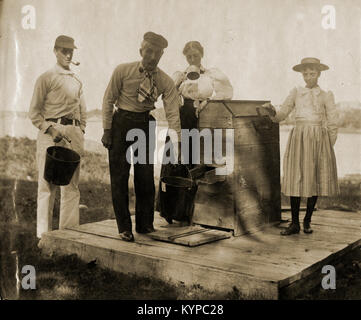 Antique circa 1905 fotografia, la famiglia a pompa acqua con fiume in background. La posizione è in o vicino a Riggsville (ora Robinhood), Maine in Sagadahoc County, Stati Uniti d'America. Foto Stock