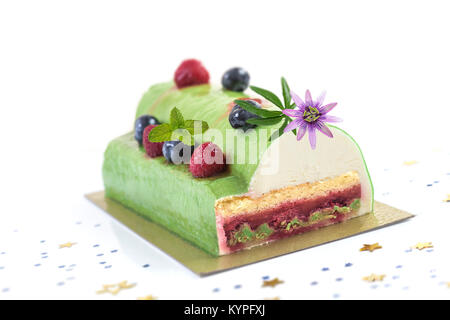 Il pistacchio Lampone Yule Log decorate con lamponi freschi, mirtillo e pasion fiore su sfondo bianco. Foto Stock