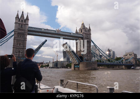 Una vista di Tower Bridge sollevato con persone prendendo fotografie scattate dal ponte di una nave da crociera fluviale, rivolta verso la città di Londra Foto Stock