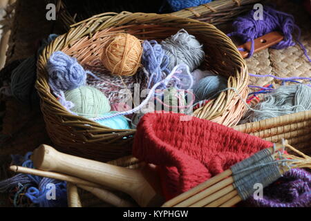 La lana o le sfere di filati e aghi di tessitura, in un tradizionale artigianato in vimini cesto Foto Stock