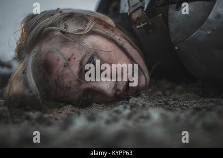 Ragazza con ferite sul suo volto nell'immagine di Jeanne d'Arc si trova nel fango in armatura. Primo piano. Foto Stock