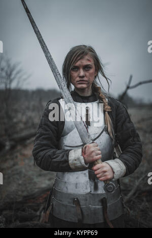 La ragazza di immagine di Jeanne d'Arc con ferite sul suo viso si erge sul prato in armatura e con la spada nelle sue mani. Foto Stock