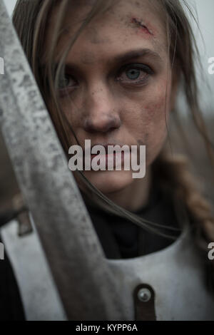 Ritratto di ragazza in immagine di Jeanne d'Arc con ferite sul suo viso in armatura e con la spada nelle sue mani. Foto Stock